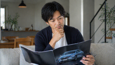 自宅で車の資料を見ながら検討している30代後半の日本人男性のリアルな様子